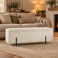 Lola ivory bouclé storage ottoman with a padded lid and slim black metal legs in a cosy living room.