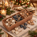Rustic wooden tray containing whitewashed, charcoal and natural wooden heart decorations with twine loops, displayed on a Christmas dining table with candles, evergreen foliage and a softly lit Christmas tree.