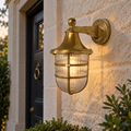 Grand Tiller Wall Lantern with brass-toned cage and ribbed glass, mounted on a stone wall beside a dark front door.